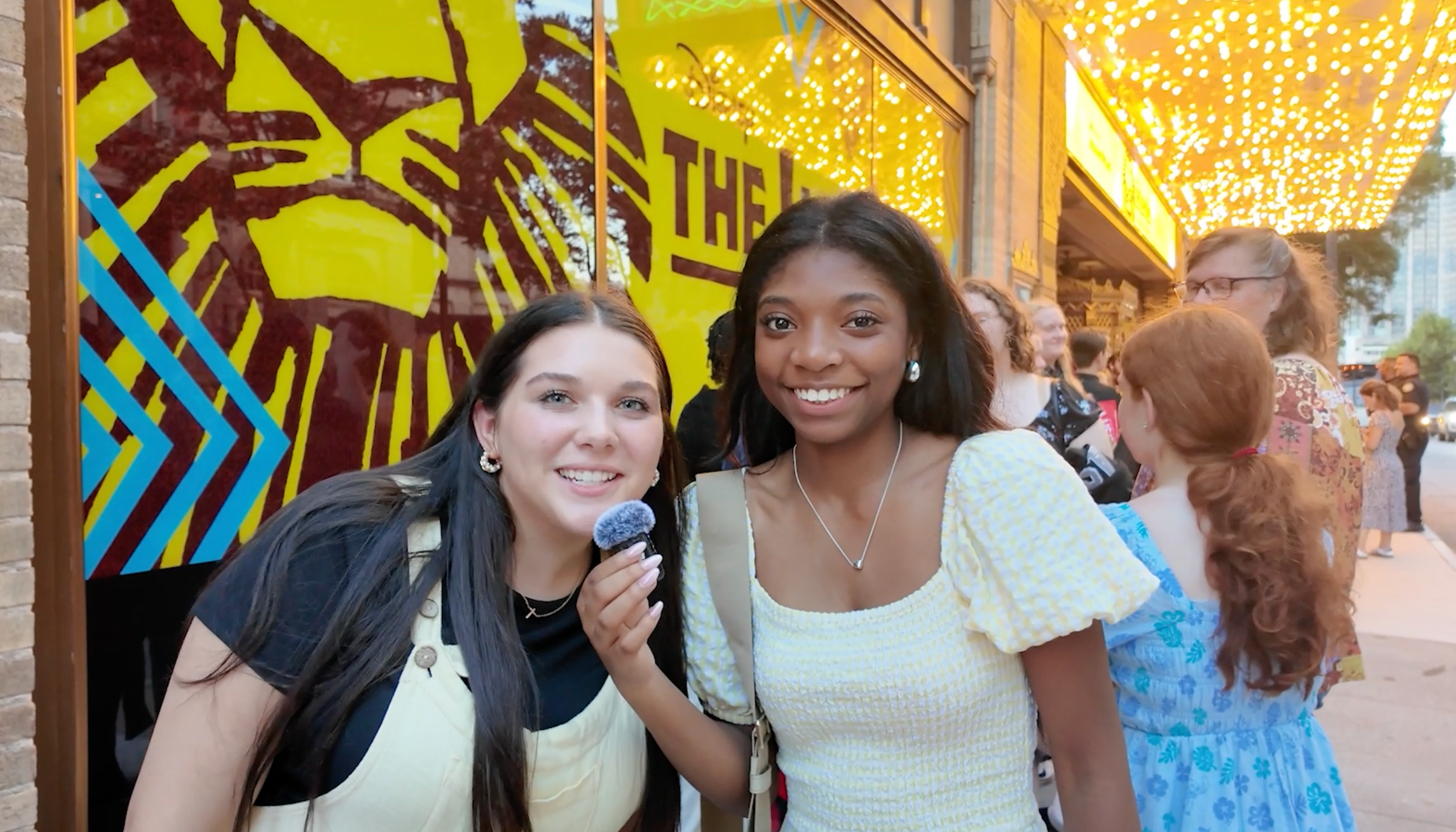 Two teens stand outside of the Fox Theatre in Atlanta. They are standing in front of a yellow "The Ling King" poster with brown text.