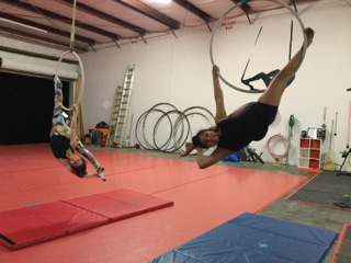 Two advanced lyra students practice their overextended splits while hanging on the lyra.
