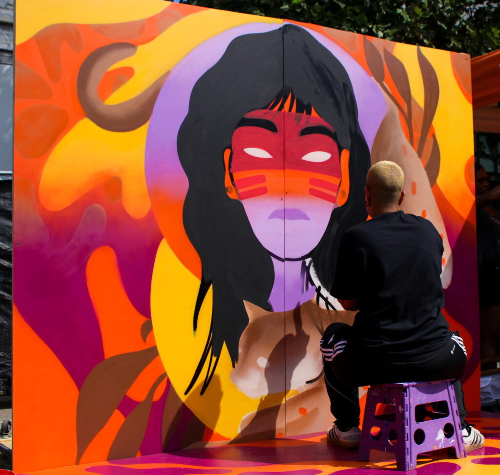 An artist creating a live painting at OYE Music Fest. The painting is purple, yellow and orange and features a person with long black hair.