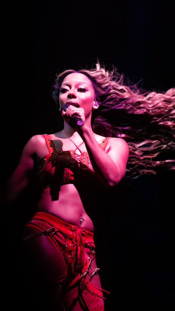 R&B artist Victoria Monét performing at ONE Music Fest 2024. Monét is wearing a red two-piece set and standing in front of a black background.