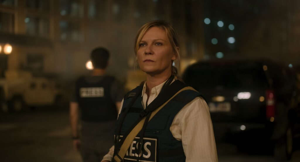 Actor Kirsten Dunst wearing a blue press badge in a still from the 2024 film, "Civil War."